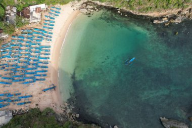 aerial view of white sandy tropical beach with blue fishing boats lined up neatly on the shore