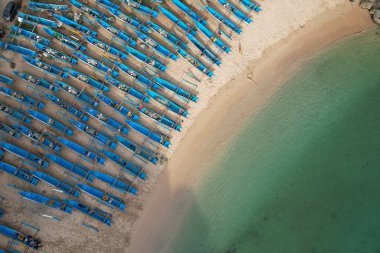 aerial view of white sandy tropical beach with blue fishing boats lined up neatly on the shore