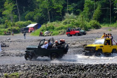 Yogyakarta, Indonesia - June 19, 2022: Off-road jeep cars drive on river. 4x4 off-road car adventure in natural terrain in Indonesia. clipart