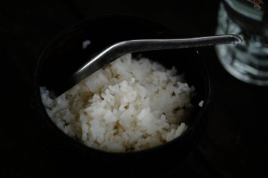 Pirinç ve kaşığı siyah kaseye koy. 