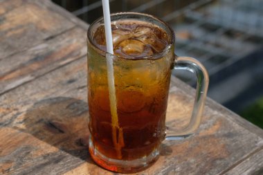 Es Teh. Buzlu çay, çay, su, şeker ve buz küplerinden yapılan taze bir içecektir. Kahverengi ahşap bir masada berrak bir bardakta buzlu çay. Endonezya içeceği.