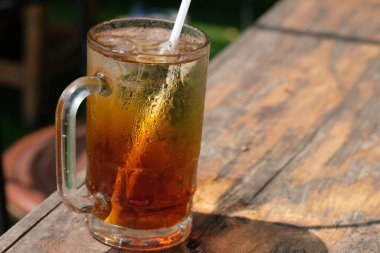 Es Teh. Buzlu çay, çay, su, şeker ve buz küplerinden yapılan taze bir içecektir. Kahverengi ahşap bir masada berrak bir bardakta buzlu çay. Endonezya içeceği.