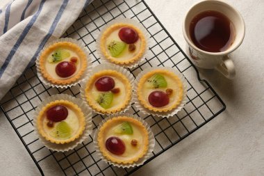 Soğutma rafında meyveli turtalar ve bir fincan çay. Lezzetli ve sağlıklı yemekler. Kivi parçaları, üzüm ve kuru üzümler var. Beyaz mermer bir masada..