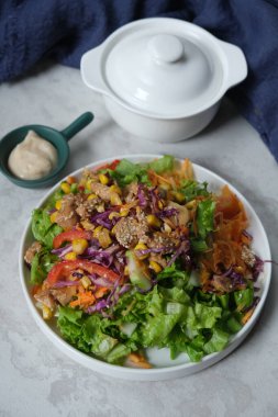 Teriyaki usulü tavuk, çiğ sebze salatası, marul dilimleri, havuç, kırmızı biber, mor lahana, haşlanmış mısır, üstüne teriyaki tavuğu ve üzerine beyaz susam tohumu serpiştirilmiş..