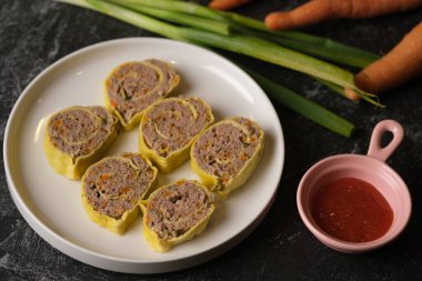 Rolade Daging Sapi. Yuvarlak beyaz seramik tabakta sığır eti Roulade. Kıyma, biber, hindistan cevizi, yumurta, sarımsak, havuç, soğan yaprağı. Domates sosuyla servis edilir..