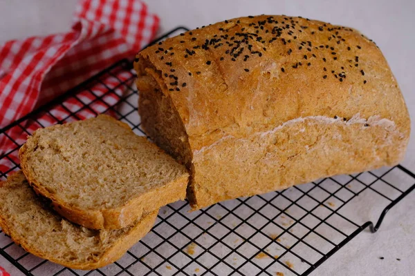 全粒小麦パンに黒ゴマをトッピング オーブンで焼いた小麦から作られています 白い大理石のテーブルの上の冷却ラックで提供されました 国内の多粒パン — ストック写真