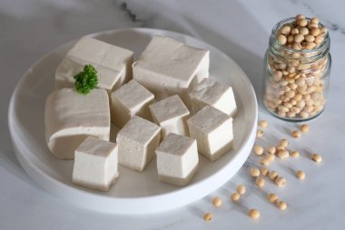 Tofu ya da soya peyniri geleneksel soya fasulyesinden yapılan yemektir. Beyaz seramik tabakta dilimlenmiş tofu. Tahu Putih. Cam kavanozda soya fasulyesi..