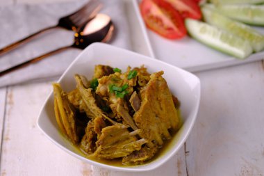 Tengkleng Kambing, baharatlar, soya sosu ve biberli, genç keçi kemiklerinden yapılan geleneksel bir Orta Cava yemeğidir. Kahverengi ahşap bir masada beyaz bir seramik kasede servis ediliyor. Endonezya yemekleri.