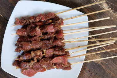 Beyaz seramik tabakta Sate Sapi bifteği satay. Satay kömürde kızarmadı. Geleneksel Endonezya yemekleri, soya soslu, sarımsaklı, biberli, sonra da şiş..