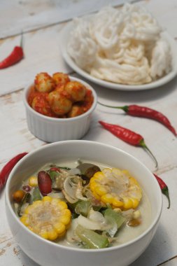 Sayur Bening Bayam ıspanak çorbası, taze ıspanak, havuç, mısır, kırmızı soğan ve defne yaprağından yapılır. Bu çorba beyaz kasede servis edilir. Endonezya yemeği. Üst manzara, düz yatak, ahşap masa.