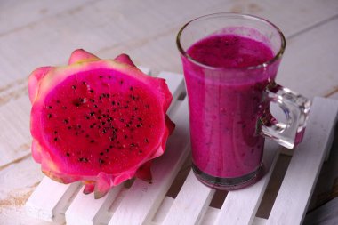 Kırmızı ejderha meyveli smoothie. Kırmızı ejderha meyve suyu. C vitamini ve antioksidan içeren ejderha meyvesinden yapılmış sağlıklı bir içecek. Sağlığa yararlı olan diyet içecekleri. Beyaz ahşap masada servis edilir..