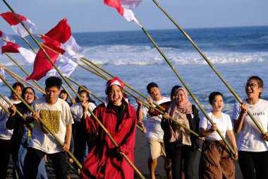 Yogya, Endonezya. 13 Ağustos 2023. Endonezya Cumhuriyeti Bağımsızlık Günü anısına plajda kırmızı ve beyaz bayrak taşıyan Endonezyalı gençler. Bendera Merah Putih. 