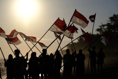 Yogya, Endonezya. 13 Ağustos 2023. Endonezya Cumhuriyeti Bağımsızlık Günü anısına plajda kırmızı ve beyaz bayrak taşıyan Endonezyalı gençler. Bendera Merah Putih. 