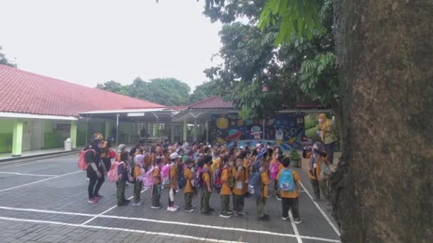スポーツの制服を着たアジア系の子供たちが学校のフィールドに並んで袋を持っていて 彼らの先生が同行しました 遠足の説明 — ストック動画