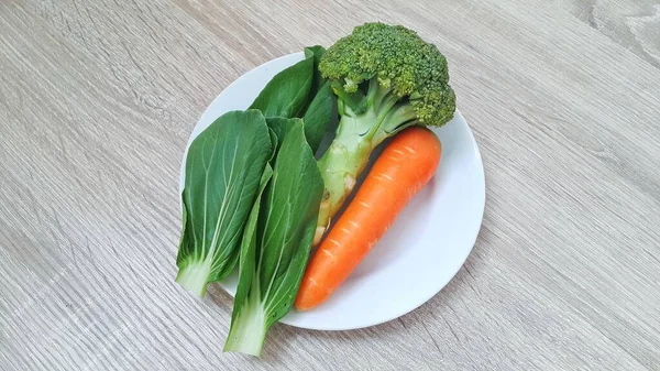 Een Bord Verse Groenten Houten Tafel Pakcoy Broccoli Wortelen Een — Stockfoto
