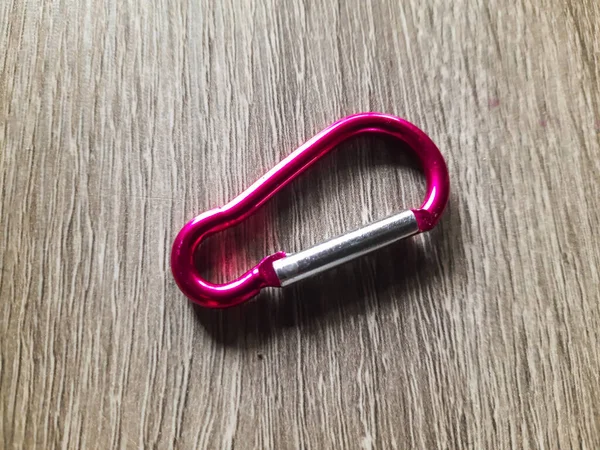 木の質感の背景に小さなピンクのカラビナ 登山用ではなく 登山用の付属品又は鍵を掛けるために使用されるキャビナー — ストック写真