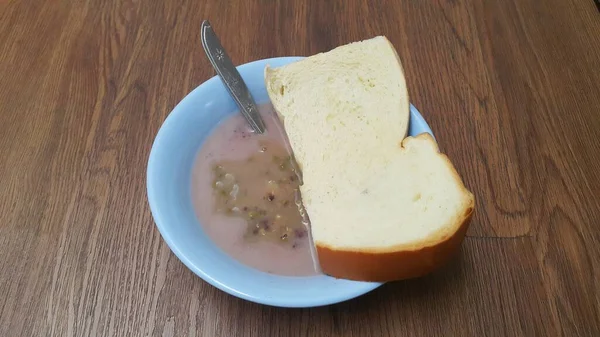 一碗绿豆粥和一块白面包放在木制背景上 — 图库照片