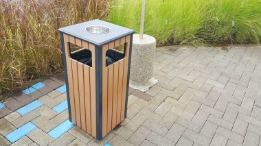 Tepesinde kül tablası olan kare şeklinde ahşap bir çöp kutusu. Açık havada..