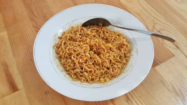 A plate of Indonesia instant fried noodles. White plate and spoon on the wooden table.