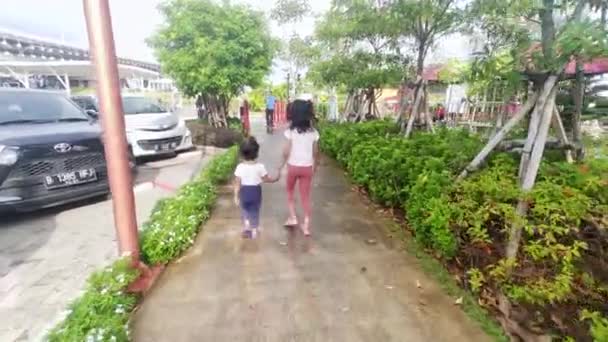 ジャカルタ北部のPik パントホーランの歩道に手をつないで歩いている2人のアジアの女の子 インドネシア ジャカルタ 2022年12月24日 — ストック動画