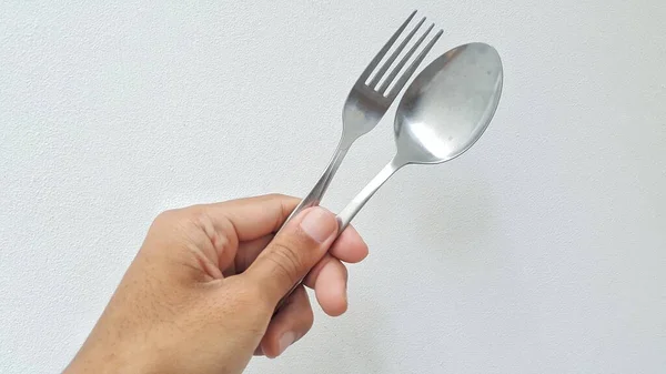 Hand holding metal spoon and fork on white background. Holding spoon and fork with one hand.