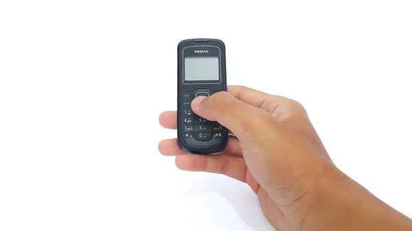 Hand holding Nokia cellphone isolated on white background. Nokia 1202 series. The old type. Jakarta, Indonesia - January 19, 2023.