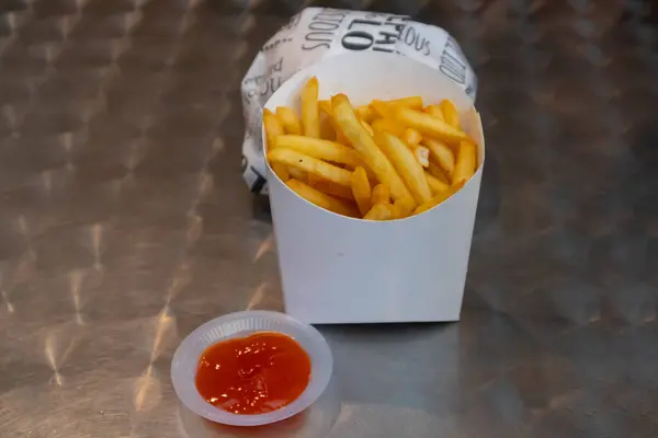 Close up view of French fries and chili sauce on the metal table