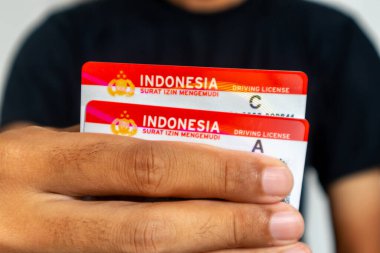 Jakarta, Indonesia - March 13, 2024: A man in black clothes holding the Indonesia driving license for car and motorcycle clipart