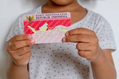 Jakarta, Indonesia - March 13, 2024: A little girl in white dress holding The Indonesian child identity card or Kartu Identitas Anak clipart
