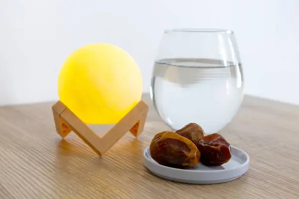 A small plate of dates fruit on a wooden table with a glass of water and lamp