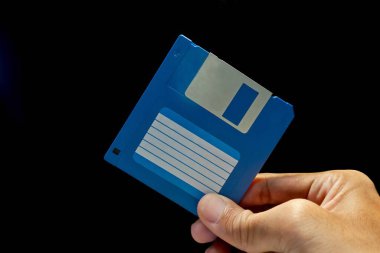 Close up view of hand holding a floppy disk on dark background clipart