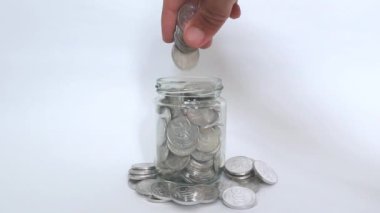 Erkek eli biriktirmek için cam bir kavanoza Endonezya Rupiah madeni parası koyar.