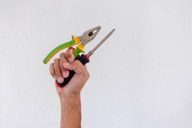Beyaz arkaplanda el ele tutuşan tornavida ve pense izole edilmiş.