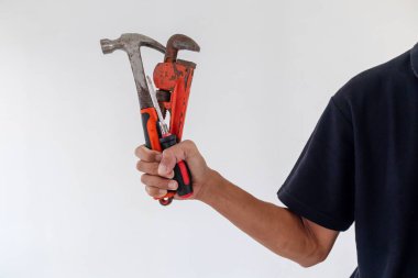 Beyaz arka planda çekiç, tornavida ve boru anahtarı tutan adam.