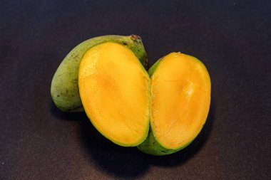 Olgun yerel Endonezya mangosunun koyu arka planda yarı izole edilmiş hali.