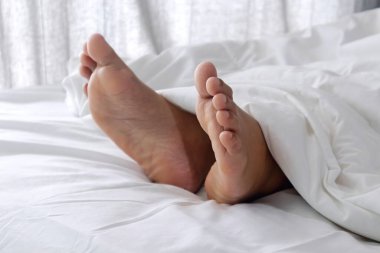 Beyaz yatakta tek başına kadın ayakları. Beyaz battaniye ve beyaz yatağın altında uyuyan bir kadın.