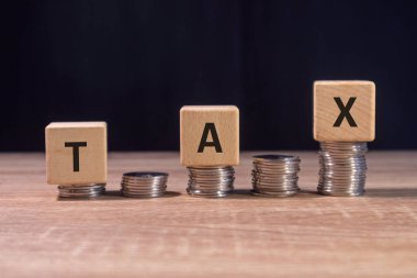 Üzerinde vergi yazan bir yığın bozuk para ve tahta bloklar. Vergi maliyetlerini artırma kavramı.