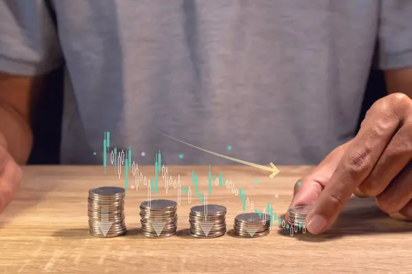 Stock image A man makes stacks of coins to calculate cost reductions. Coins stacking with the down arrow and virtual charts.