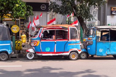 Jakarta, Endonezya - 10 Ağustos 2024: Endonezya bayrağıyla süslenmiş bir Bajaj Jakarta 'da yol kenarına park edilmiştir. Üç tekerlekli toplu taşıma.
