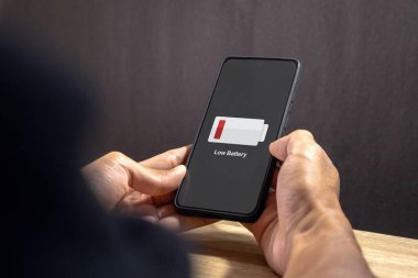 Ekranda düşük pil sembollü bir cep telefonu tutan adam.