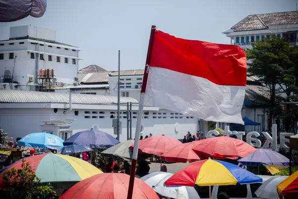 stock image Jakarta, Indonesia - August 18, 2024: An Indonesian red and white flag flutter among the umbrellas of street vendors' carts at Kota Tua Jakarta