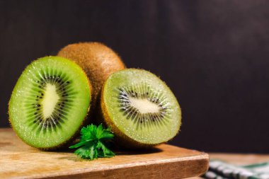 Koyu arkaplanda, ahşap masa üzerinde kivi dilimleri olan yeşil kivi meyvesi.