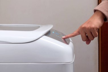 Çamaşır makinesi kullanan bir kadın. Çamaşır makinesinin düğmesine elle bas..