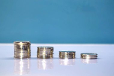 Mavi arka planı olan beyaz masaya para yığını. Seviye göre sıralanır.