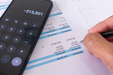 Cep telefonundaki hesap makinesi uygulamasını kullanarak elinizi kalem tutarak finansal verileri hesaplayarak kapatın. Mali rapor verilerini analiz eden bir muhasebeci.