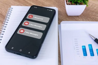 Ofis masasında cevapsız arama ve telefon ekranında yeni mesaj bildirimi olan bir akıllı telefon.
