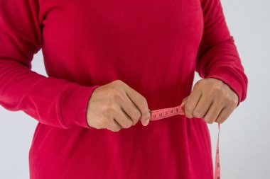 Kırmızı uzun kollu tişörtlü bir kadının yakın çekim görüntüsü bel çevresini pembe bant ölçüsüyle ölçüyor. Vücut ağırlığı kontrolü veya diyet konsepti.