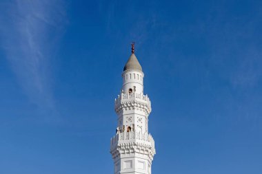 Beyaz bir cami minaresi, parlak mavi bir gökyüzü arka planına karşı.