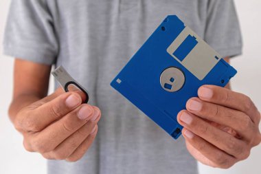 Sağ elinde USB bellek ve sol elinde disket tutan bir adam.