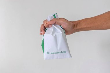 Hand holding a paper air sickness bag on white background clipart